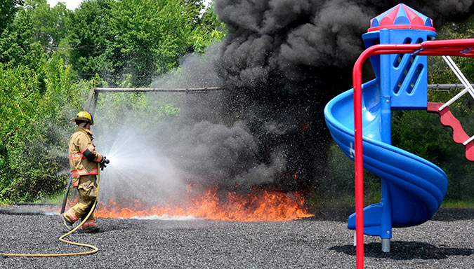 A Beaver Dam firefighters begins to spray the burning pulverized rubber mulch at the playground equipment at Oldham Park Monday afternoon in Beaver Dam.