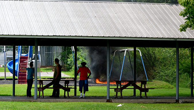 Bystanders watch as Beaver Dam firefighters arrive at Oldham Park Monday afternoon responding to the burning pulverized tire mulch at surrounding the playground equipment at Oldham Park.